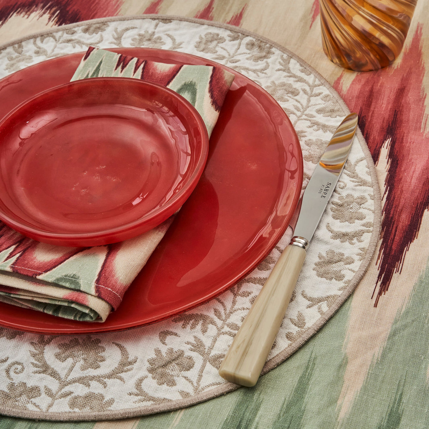 Aurora Flamestitch tablecloth in green and red ombre, Permanent Resident suzani Placemat in beige and Caju red glass dinner plate