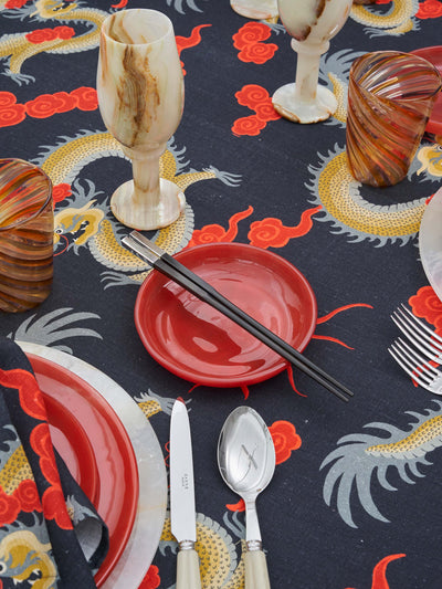 Kowloon Dragon Tablescape featuring a golden ombré dragon set against an onyx background and surrounded by red clouds, hoping to bring all good fortune and joy. Table Styles with red glass plates and Caju onyx wine glass. Linens made from Organic cotton linen and GOTS Certified.